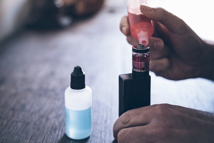 Hände, die mit Aroma für E-Zigaretten ein Liquid in einer Vape mischen