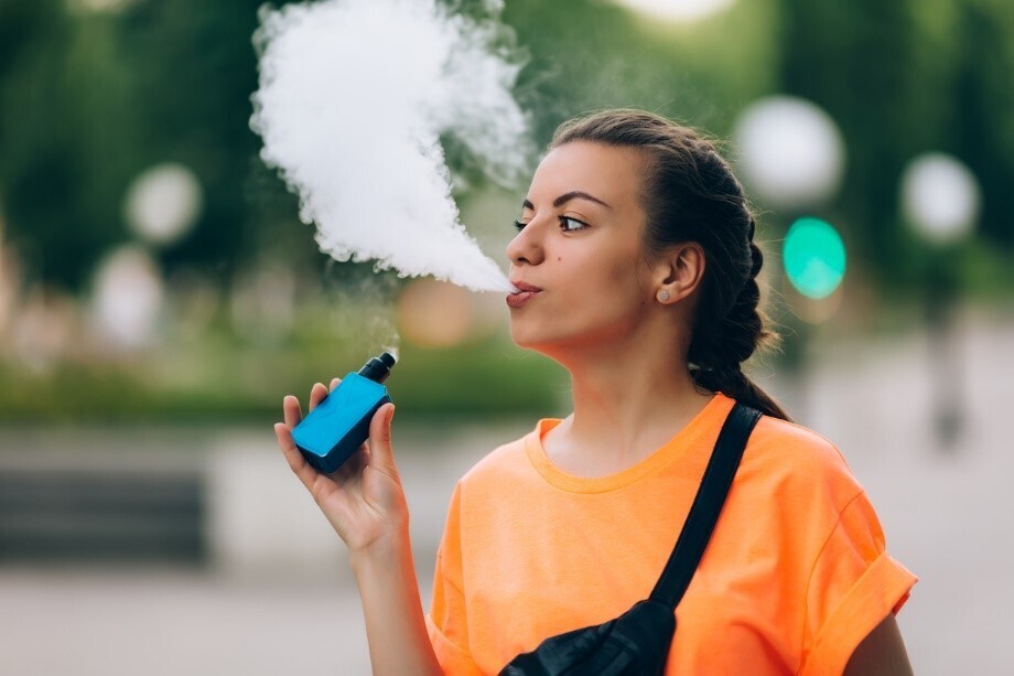 Junge Frau dampft draußen eine blaue Vape