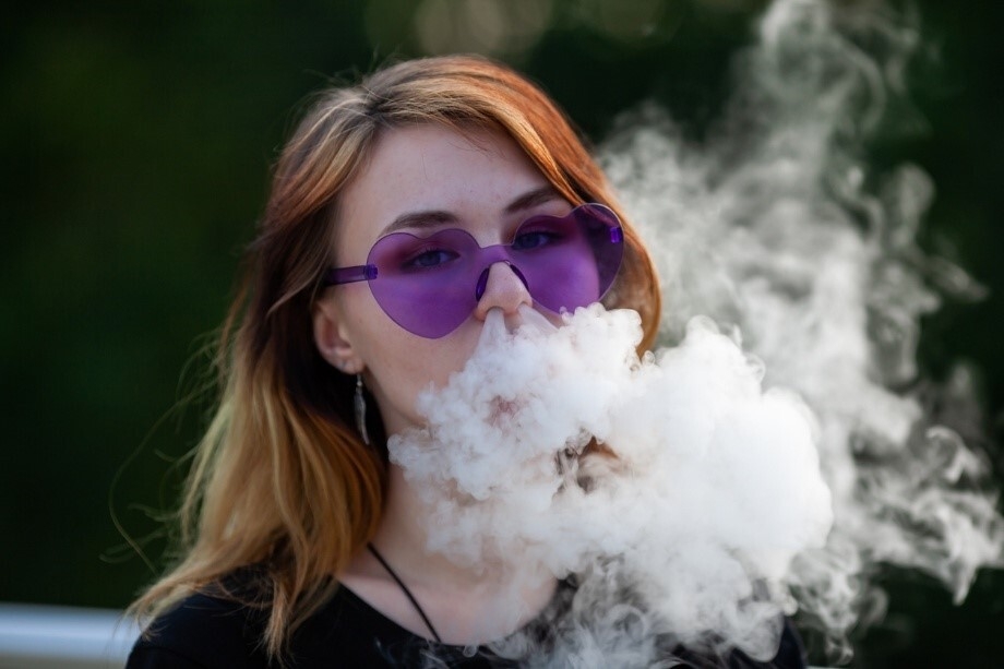 Junge Frau mit herzförmiger Sonnenbrille, die Vape-Dampf ausatmet
