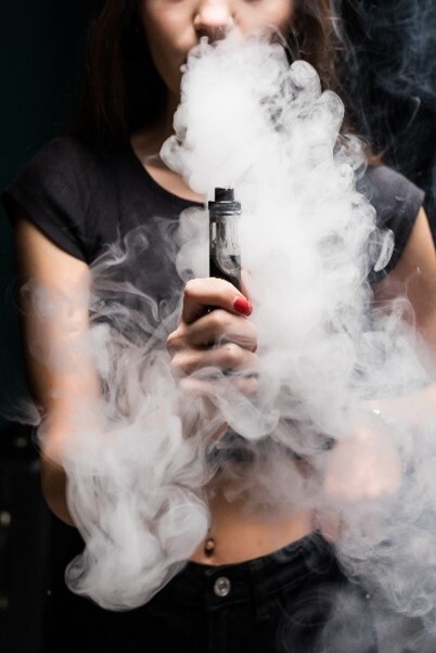 Von Dampf umgebene Frau, die eine mit Liquid befüllte Vape hält