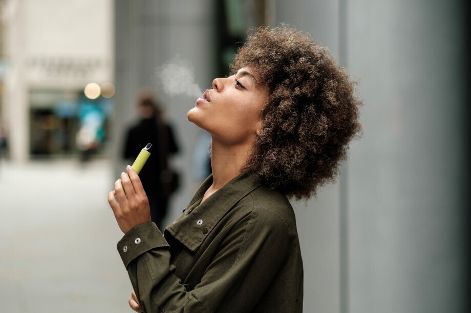 Frau atmet Dampf einer Vape vor einem Gebäude in der Stadt aus