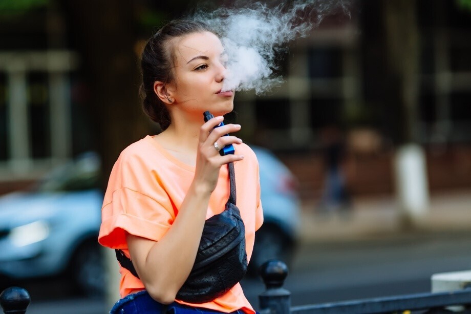 Frau, die Vape-Dampf ausatmet, überquert eine Straße