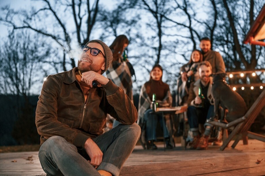 Mann nutzt eine E-Zigarette bei einem Abend mit Freunden auf einer Terrasse