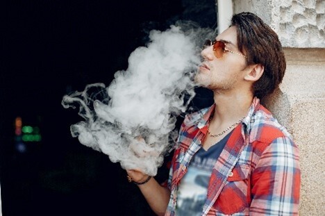 Mann, der sich an eine Hauswand lehnt und eine Vape raucht