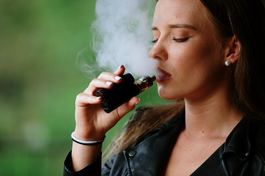 Frau, die draußen eine Vape hält und Dampf ausatmet