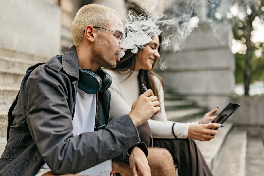 Mann, der Dampf einer Vape ausatmet, sitzt neben einer Frau