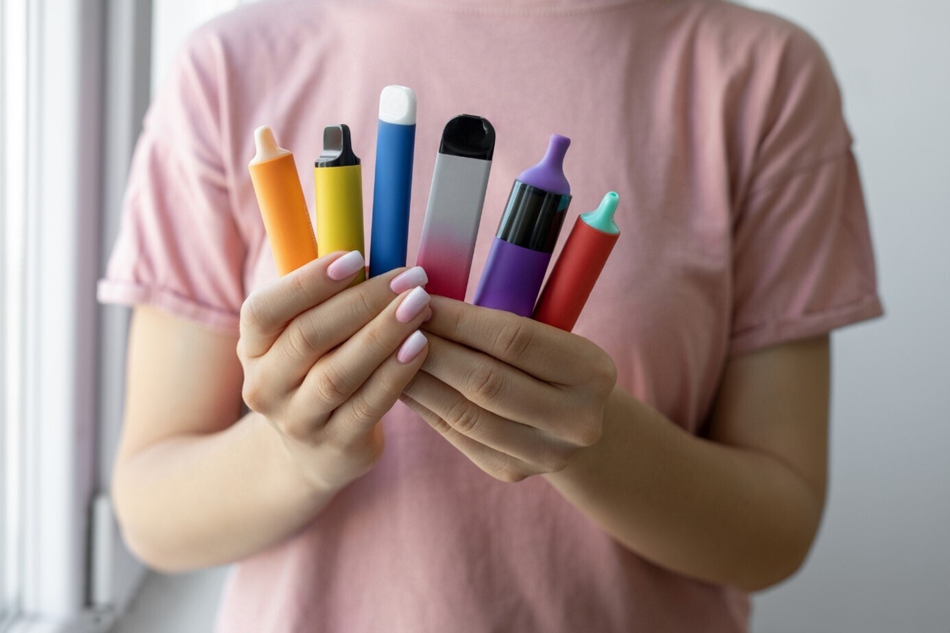 Verschiedene, bunte E-Zigaretten in den Händen einer Frau, minimalistischer Hintergrund.