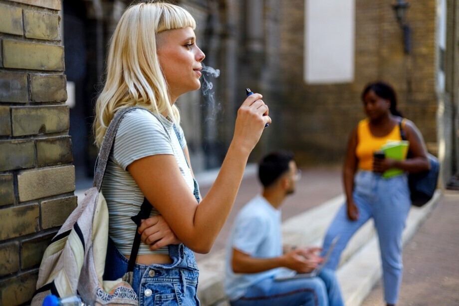 Frau, die vor dem Eingang eines Gebäudes eine Vape raucht