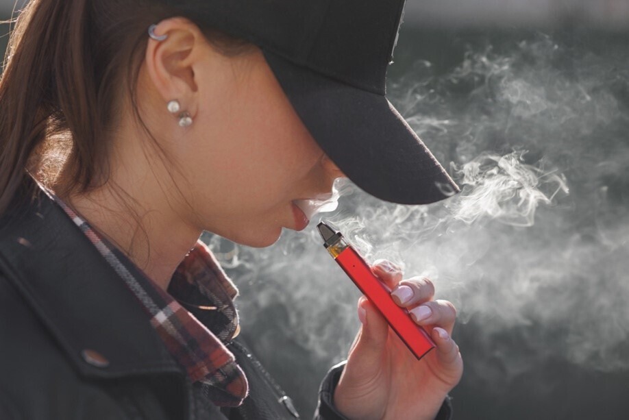 Frau, deren Gesicht von einer Baseballcap verdeckt wird, raucht eine Vape