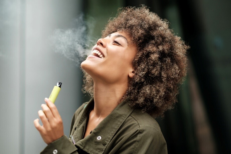 Frau lacht und dampft eine Mehrweg-Vape