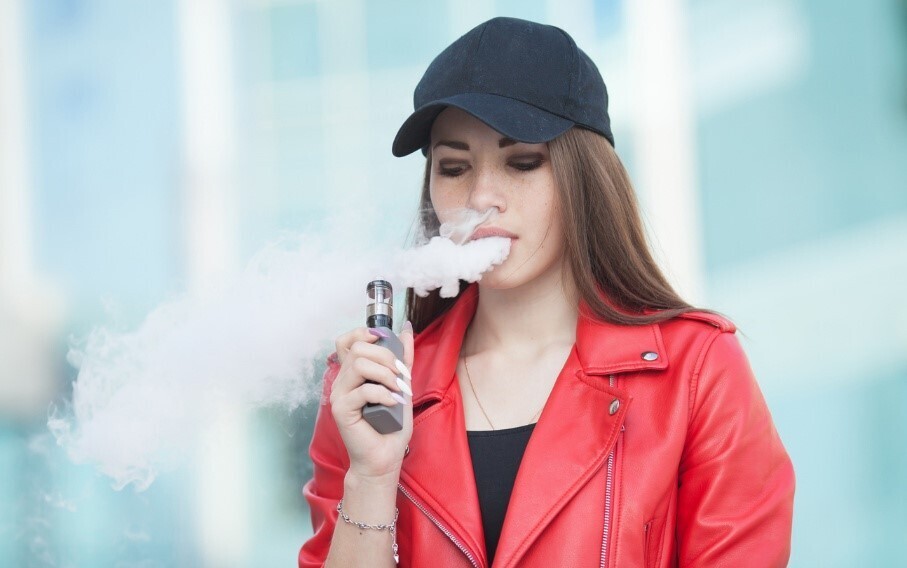 Frau in roter Jacke mit Baseball-Cap raucht eine Vape
