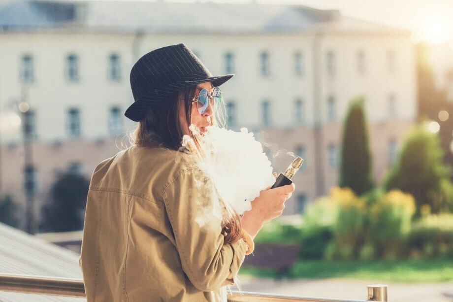Frau auf Balkon, die mit einer aufladbaren Vape dampft