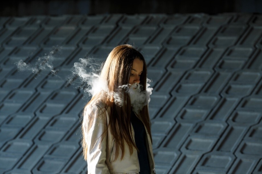 Junge Frau, die E-Zigaretten-Dampf ausatmet