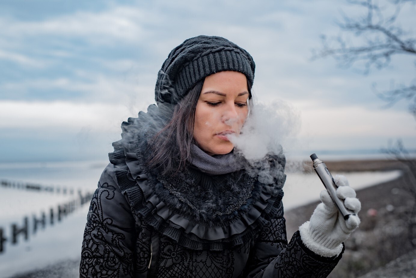 Frau mit Mütze, Handschuhen und Wintermantel am Dampfen vor einem winterlichen, verschneiten Hintergrund.